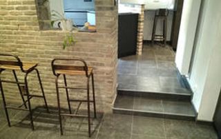 intérieur rénové avec mur en briques, bar en maçonnerie et deux tabourets, sol en carrelage gris